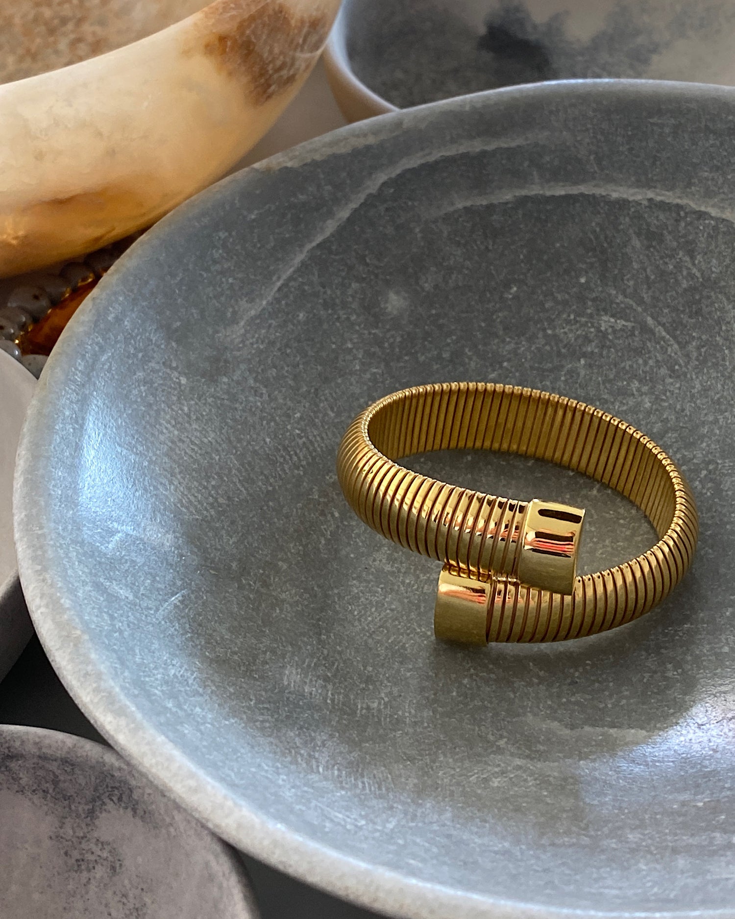 Striped wrap style gold cuff sits in a bowl