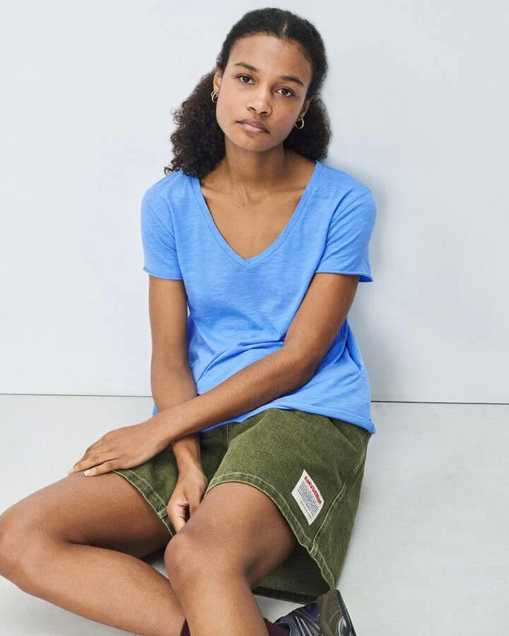Person wearing a blue shirt and green shorts sitting against a white wall.