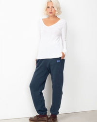 Woman wearing a white long-sleeve top and navy sweatpants with a logo on a white background
