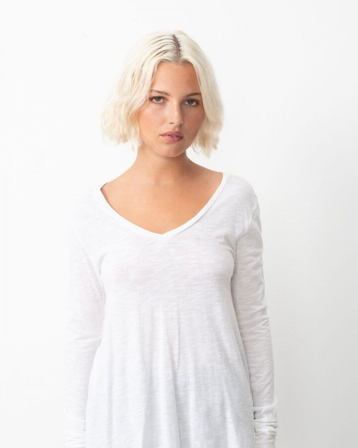 Woman wearing a white long-sleeve top against a plain background