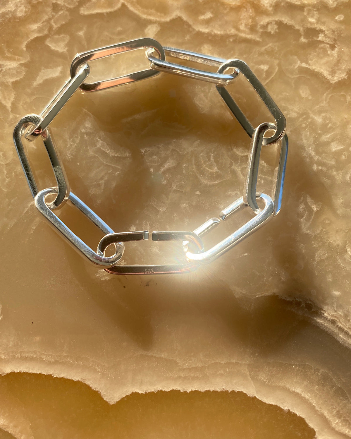 closeup of a silver curved chain link bracelet against a stone board