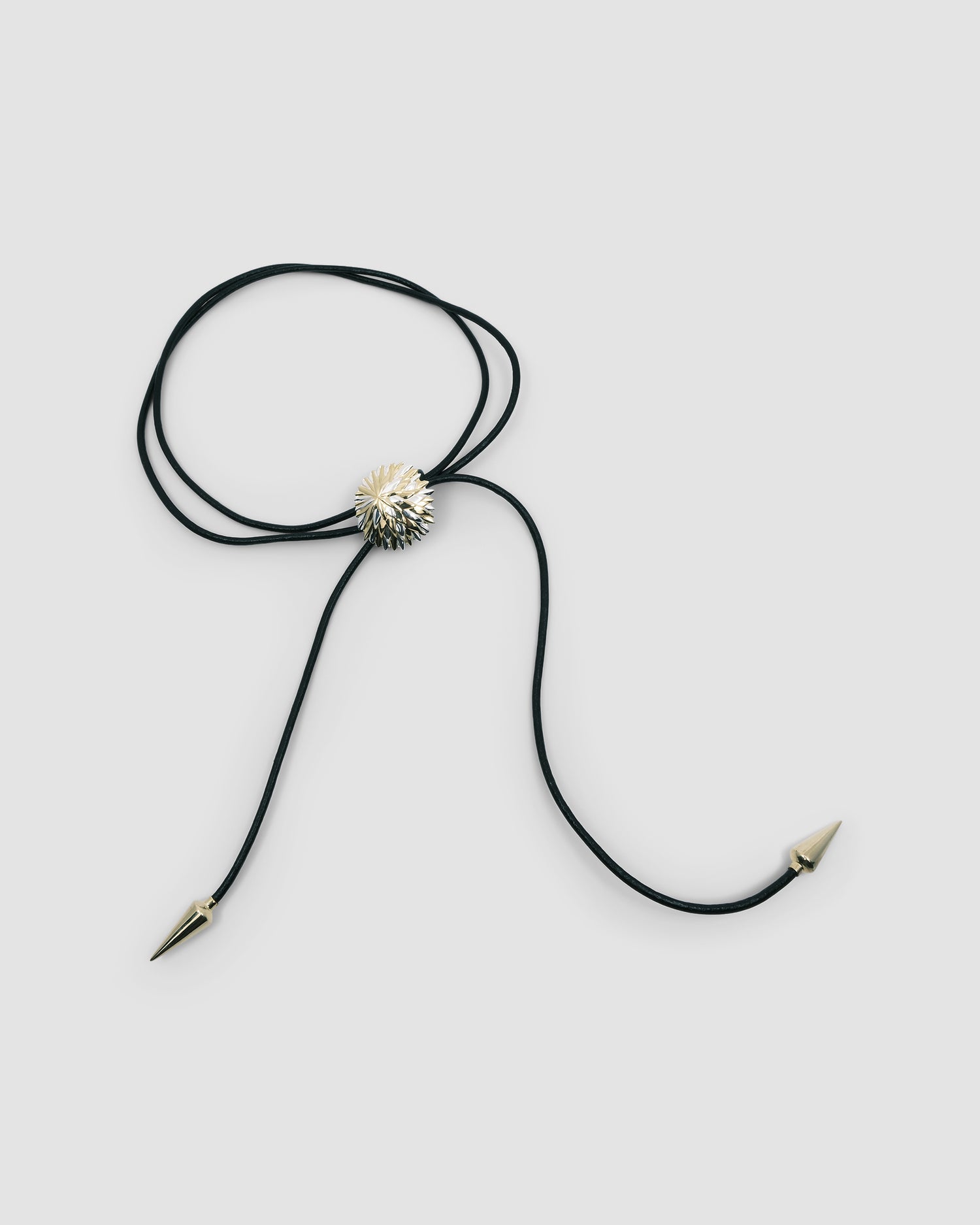 A black leather lariat with pointy gold ends and a featured mixed metal flower in the centre