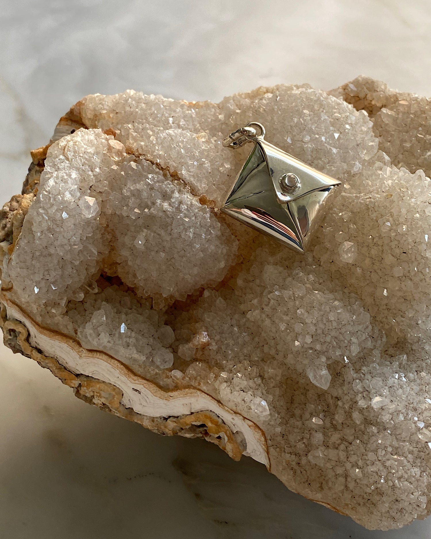 Silver charm in the shape of an envelope with a moonstone clasp sits on top a large crystal