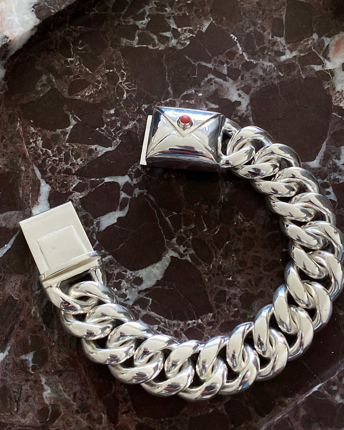 silver cuban link bracelet with a coral embellished envelope on a marble platter