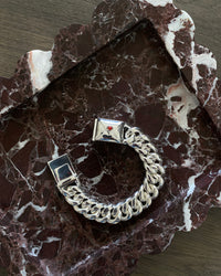 silver cuban link bracelet with a coral embellished envelope on a burgundy marble platter