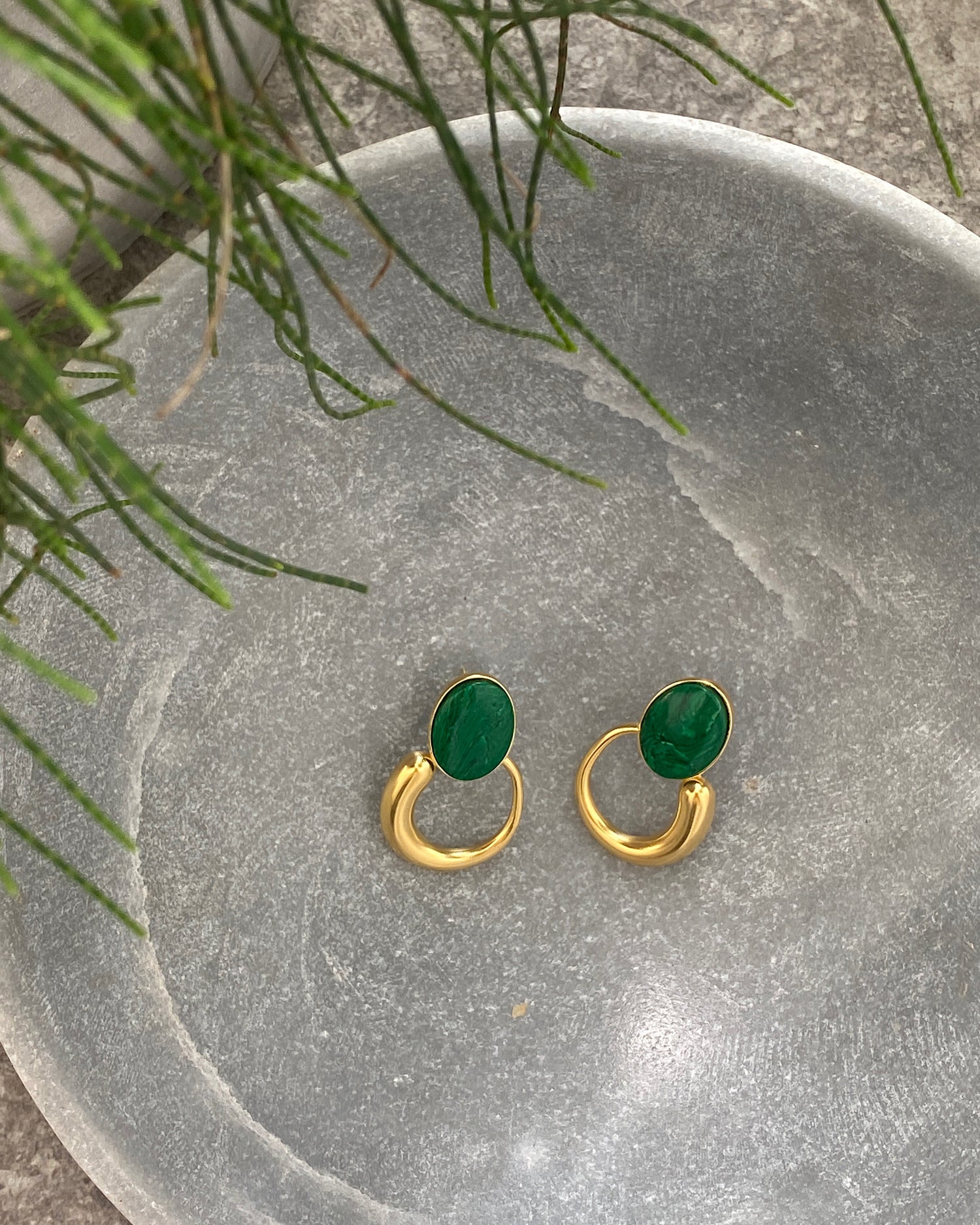 Green stone studs earrings with gold irregular hoops hanging off the bottom in a stone bowl
