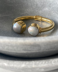 two uneven natural white baroque pearls sit at the end of a gold open cuff