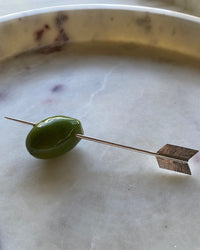 an olive sits on an arrow cocktail pick