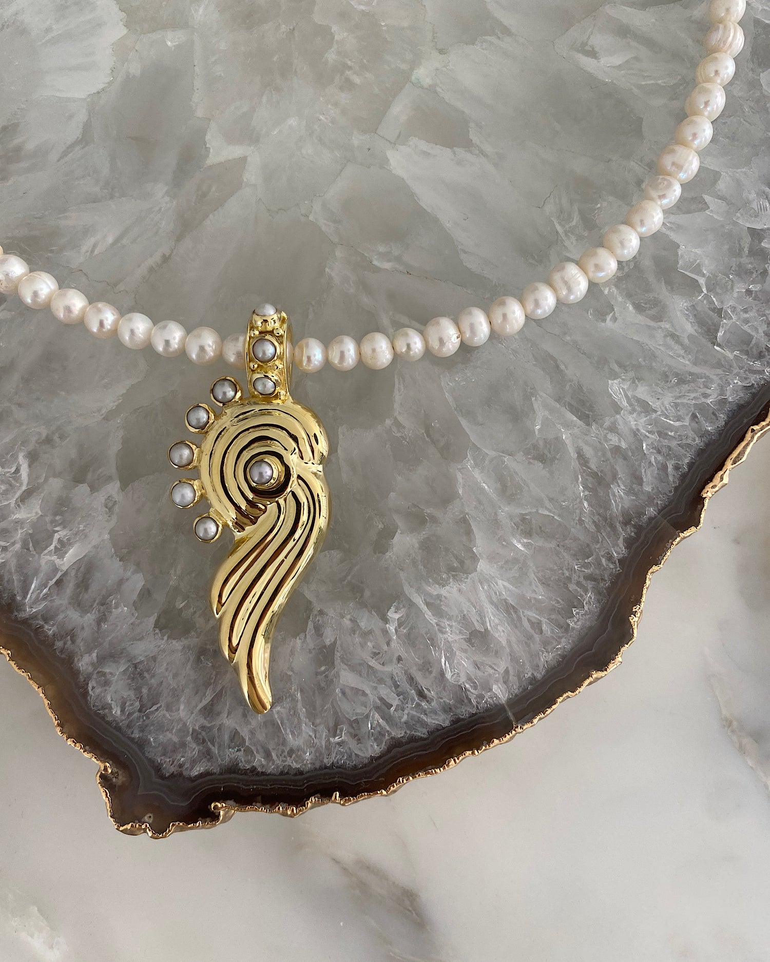 a gold swirl pendant is adorned with pearls and hangs from a pearl necklace