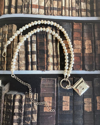 pearl necklace with a silver charm ring attached and an envelope charm on a magazine page