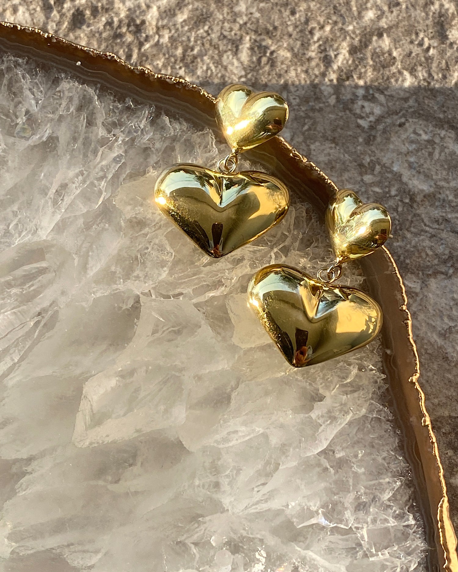 gold double heart drop earrings on a stone platter