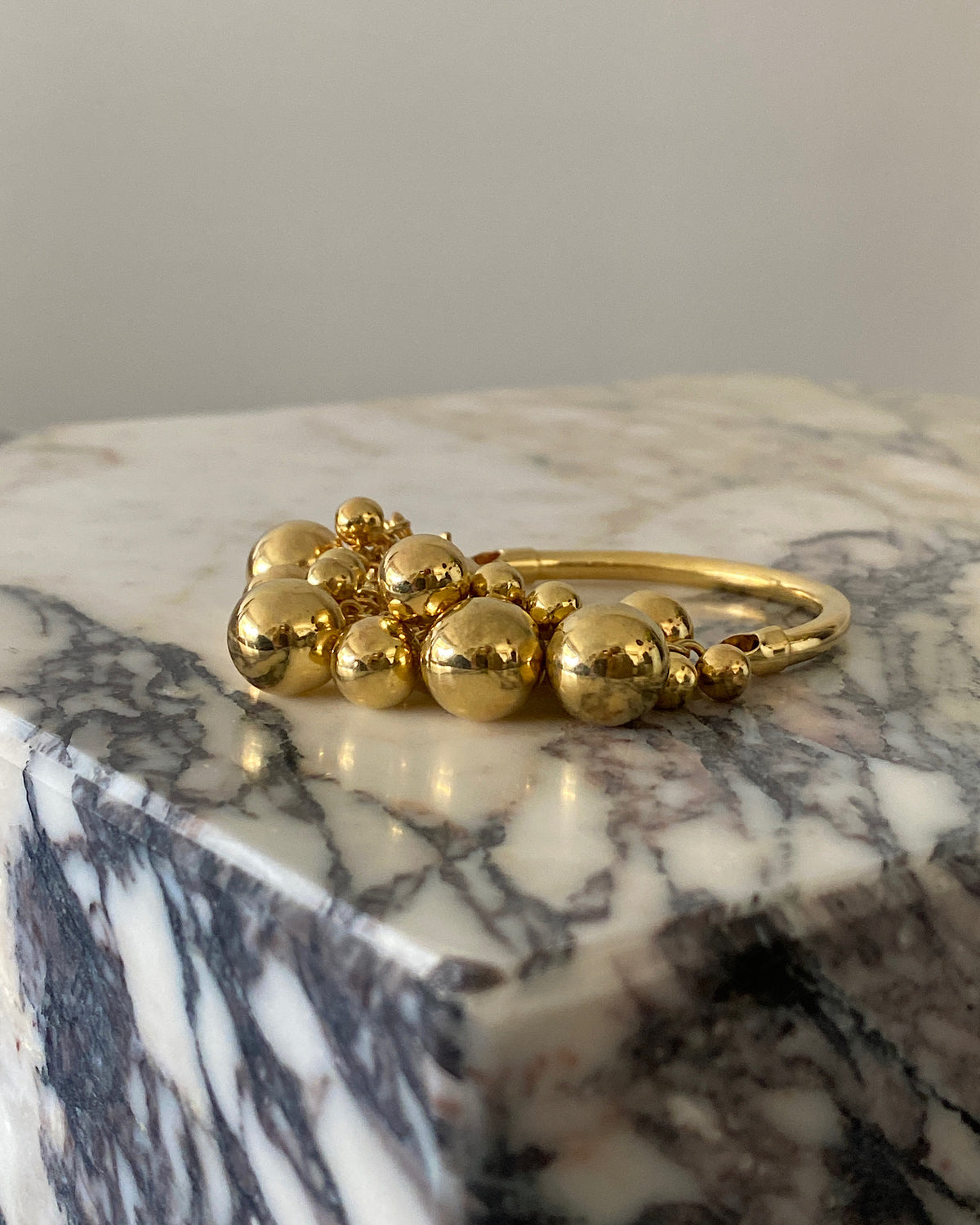 a thin gold bracelet with a group of ball charms on one side sits on a marble plinth