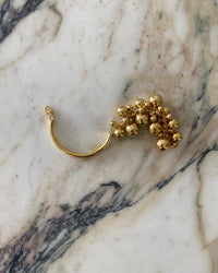 a thin gold bracelet with a group of ball charms on one side sits on a marble plinth