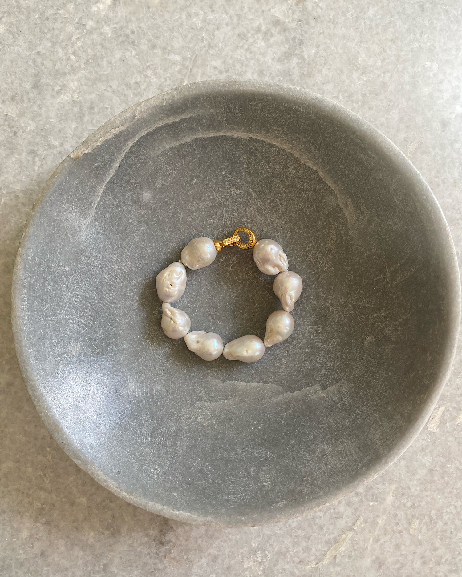 a baroque pearl and gold clasp bracelet sits in a bowl