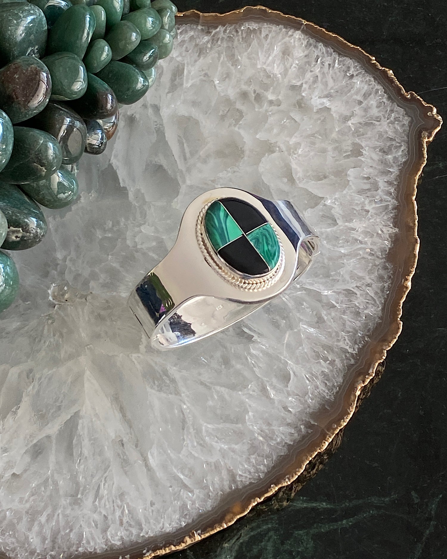 silver cuff bracelet with an inlaid black and green stone on a crystal platter