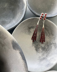 Silver Drop earrings featuring 3 coral beads and a hanging red abalone fan shaped pendant resting in a mottled grey bowl