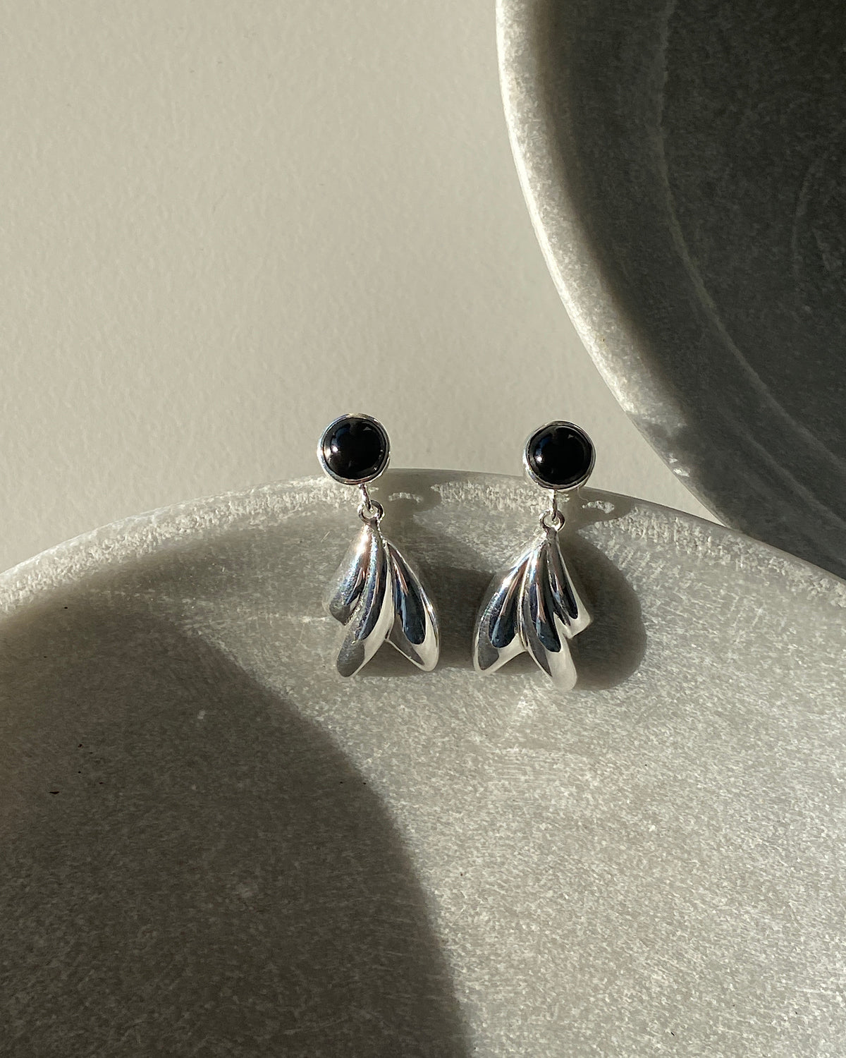 black onyx and silver sculptural drop earrings in a stone bowl