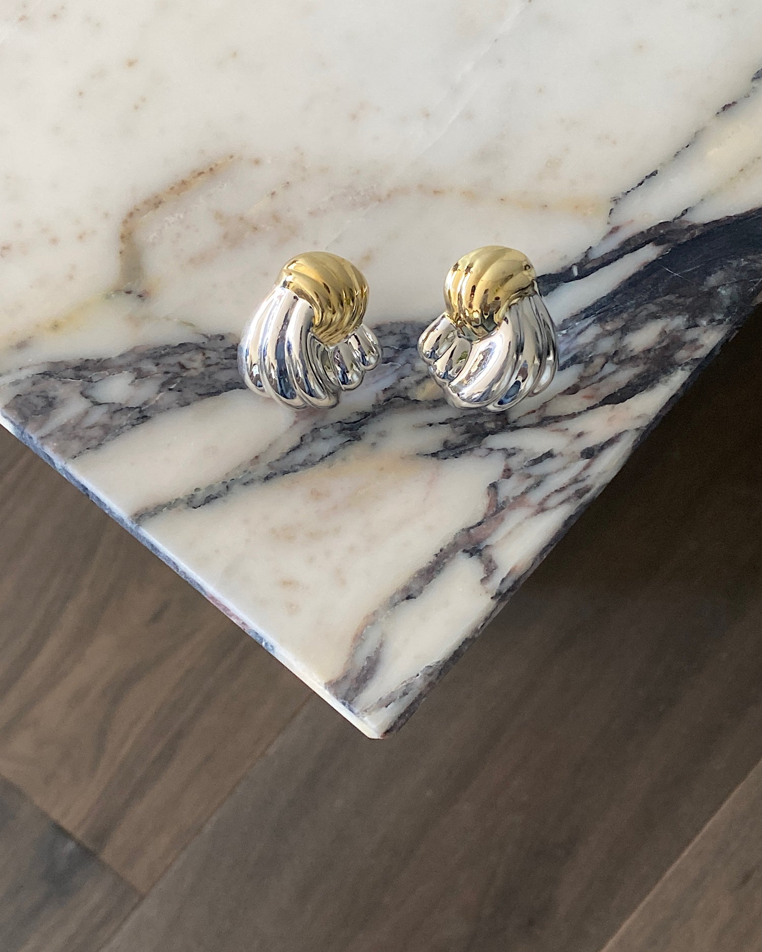 Twisted silver and gold earrings sit on a marble plinth