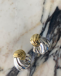 Twisted silver and gold earrings sit on marble