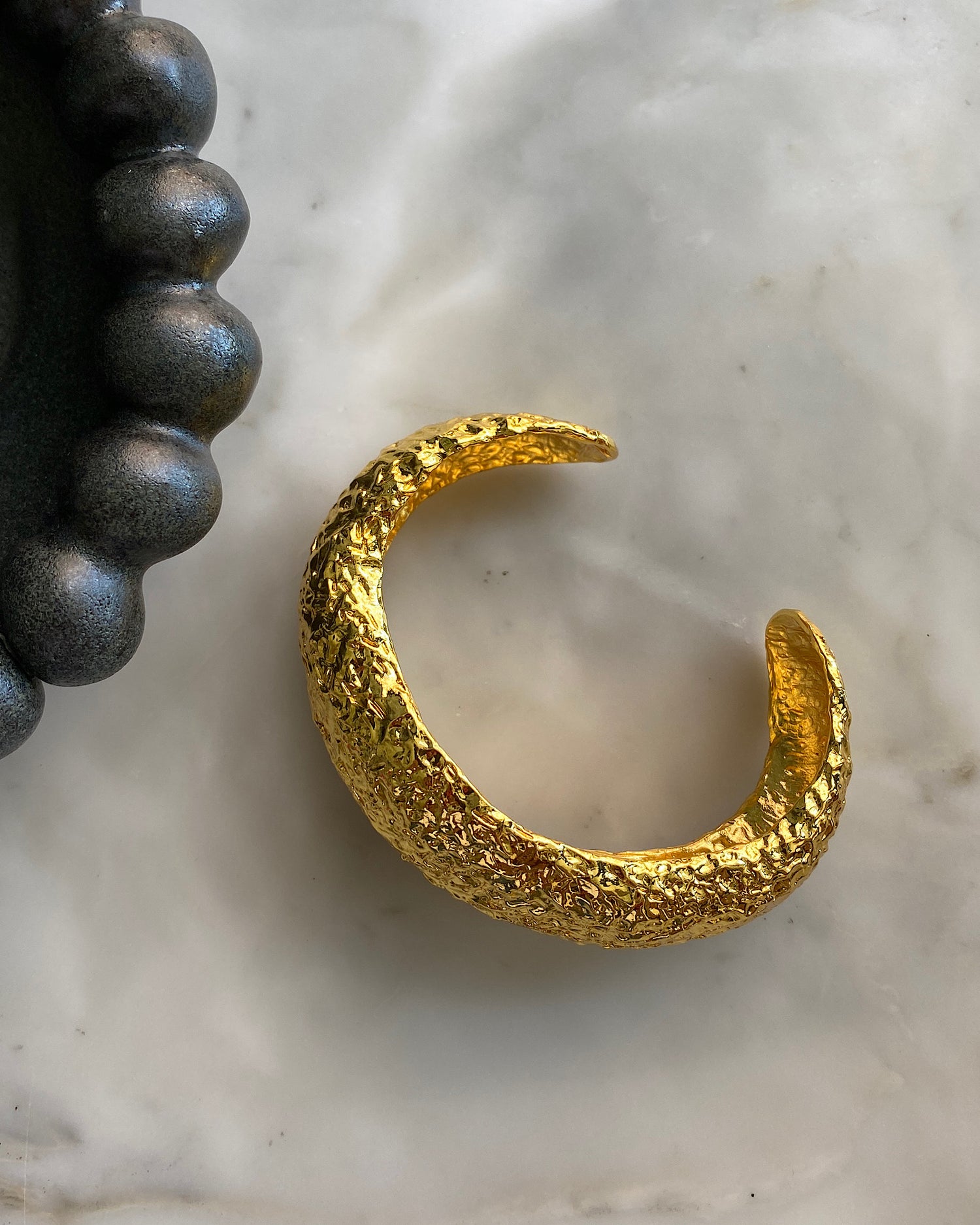 textured organic uneven wide gold cuff bracelet on a marble bench