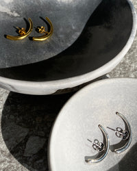 Curved silver & Curved gold bar earrings lie in two separate grey toned mottled ceramic bowls