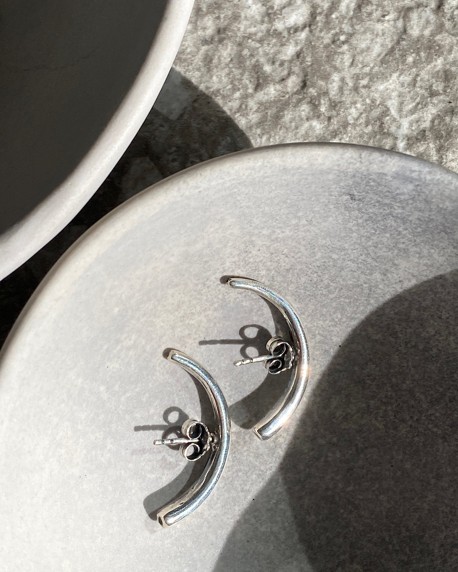 curved silver bar earrings lie in a bowl