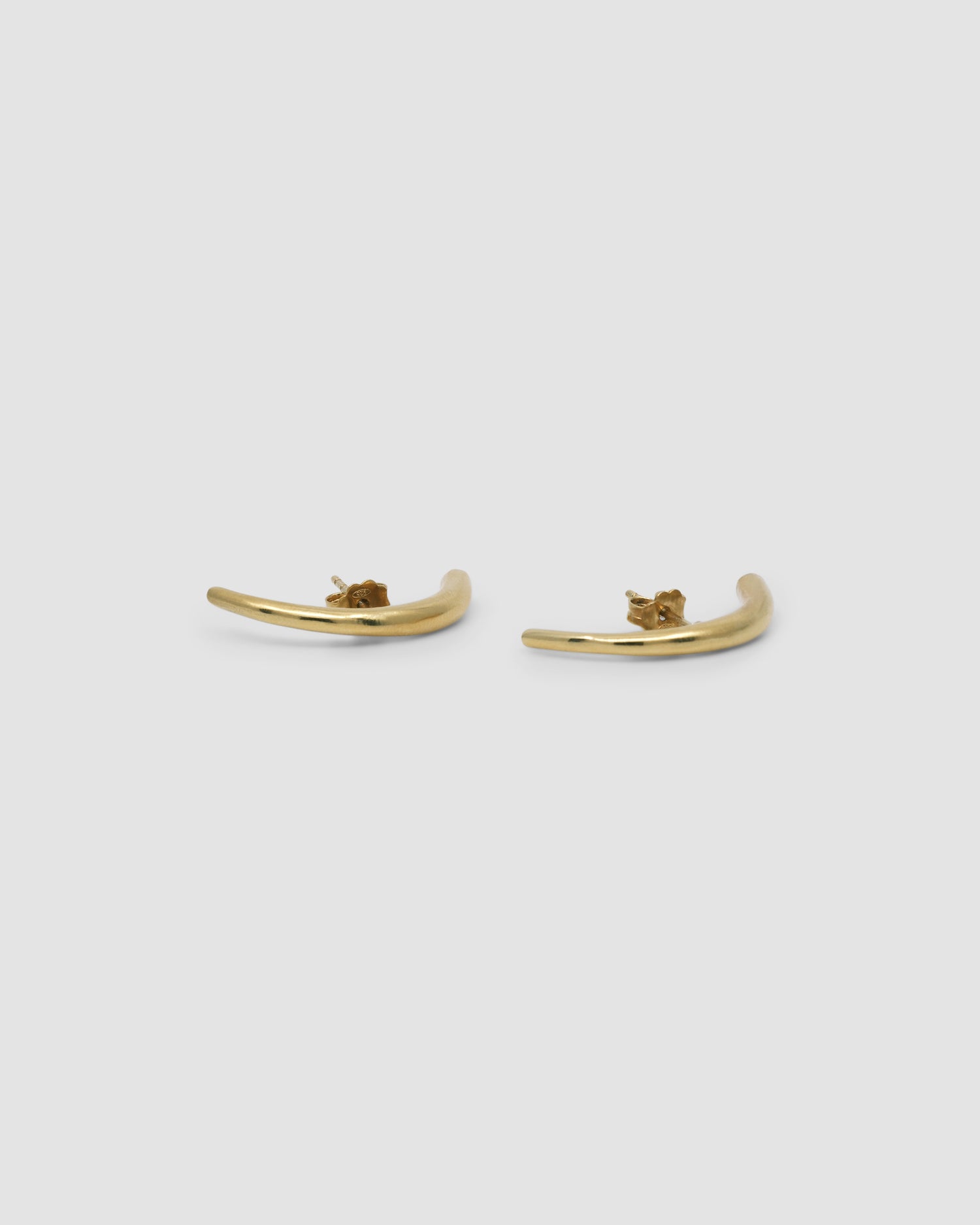 Elongated gold curved bar earrings lie on a grey background