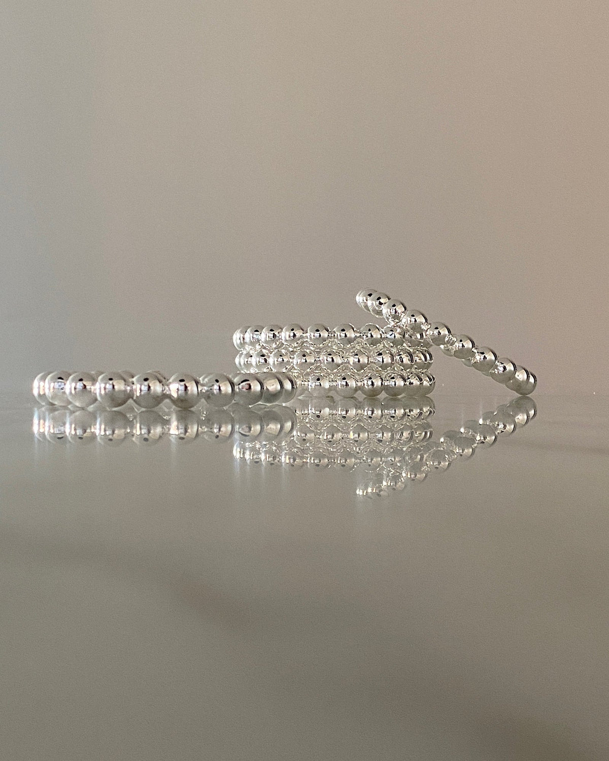 a stack of silver ball bangles sits on a marble table with reflection