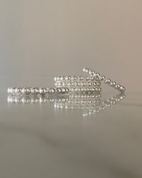 a stack of silver ball bangles sits on a marble table with reflection