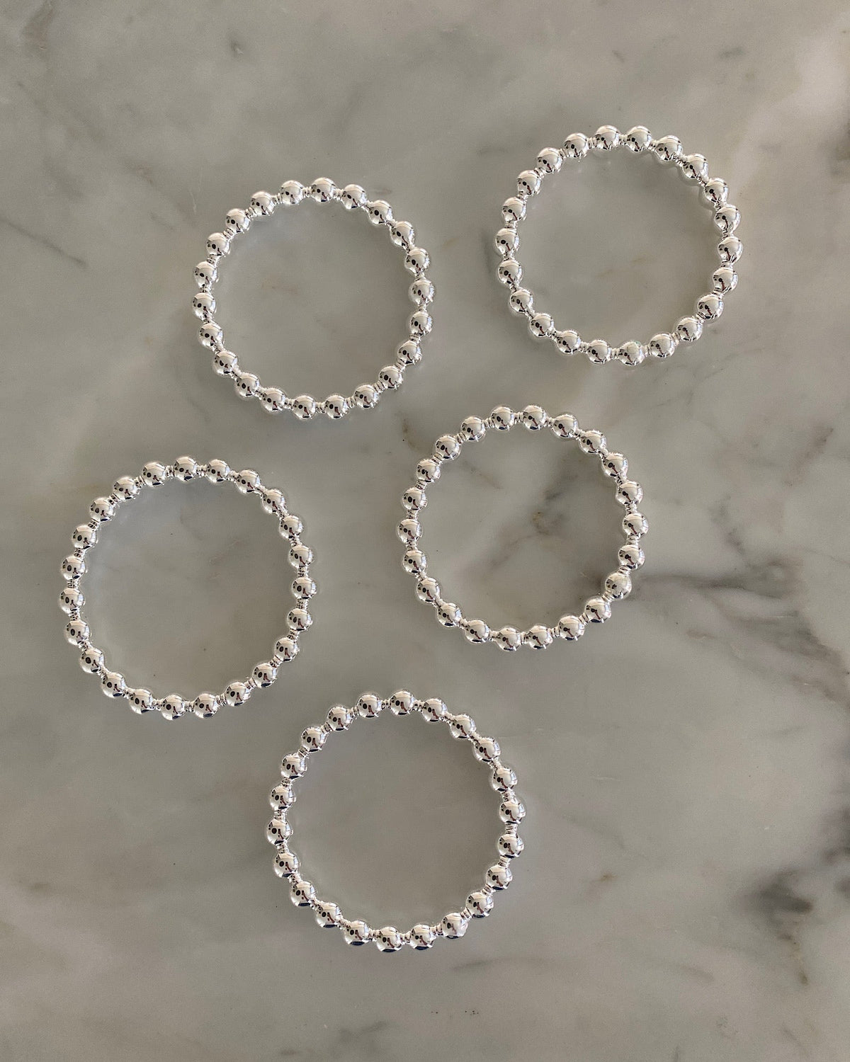 5 bangles made of joined balls sits on a marble background