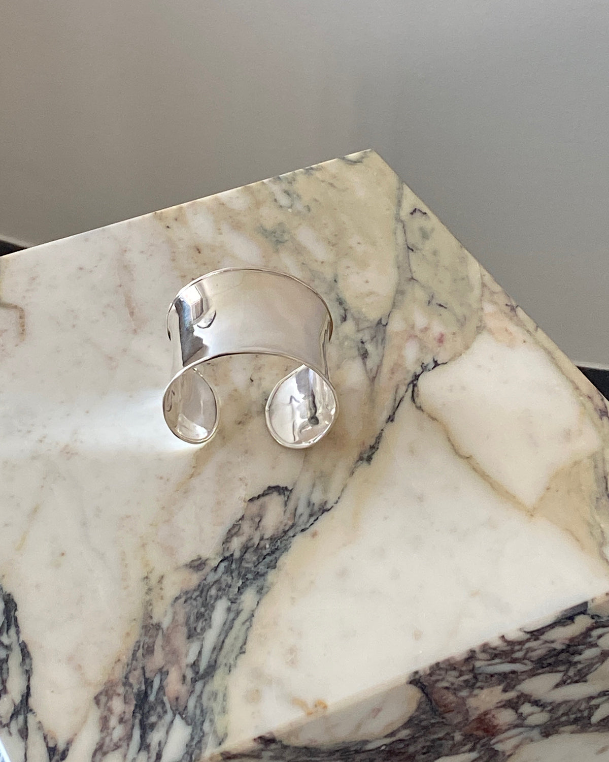 a super wide open sterling silver cuff bracelet sits on a marble plinth