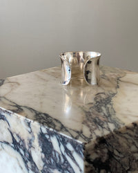 a super wide open sterling silver cuff bracelet sits on a marble plinth