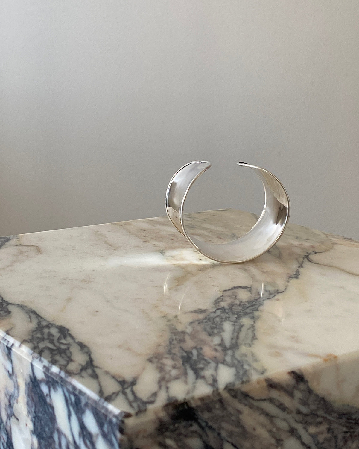 a super wide open sterling silver cuff bracelet sits on a marble plinth