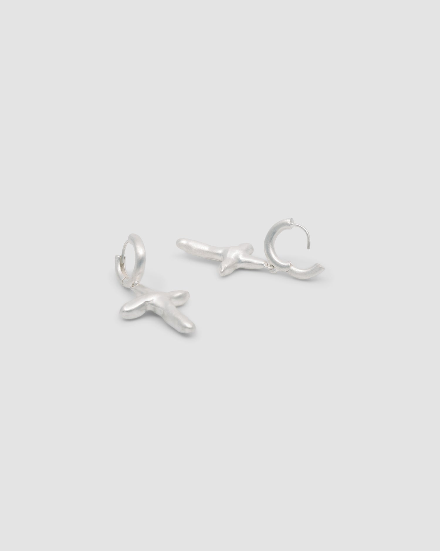 Silver matt organic shaped crosses hang from a silver huggie style earring