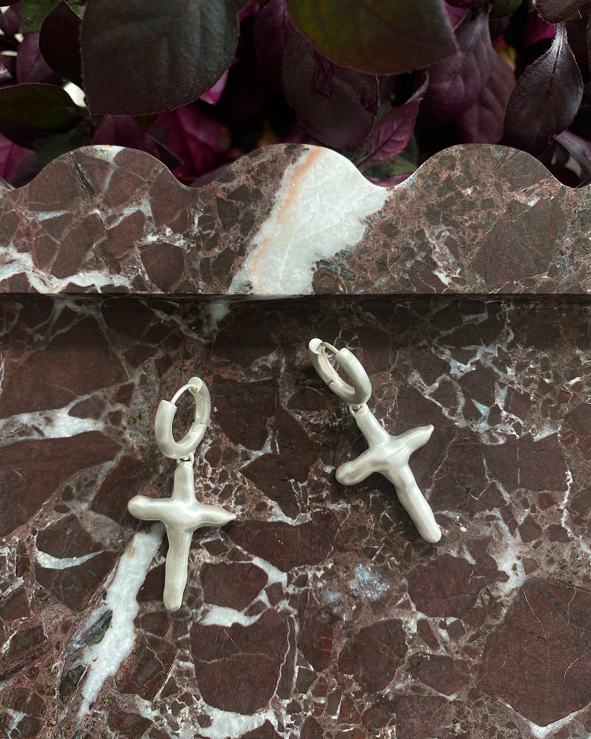 Matt silver organic cross charms suspended on a huggie style earring