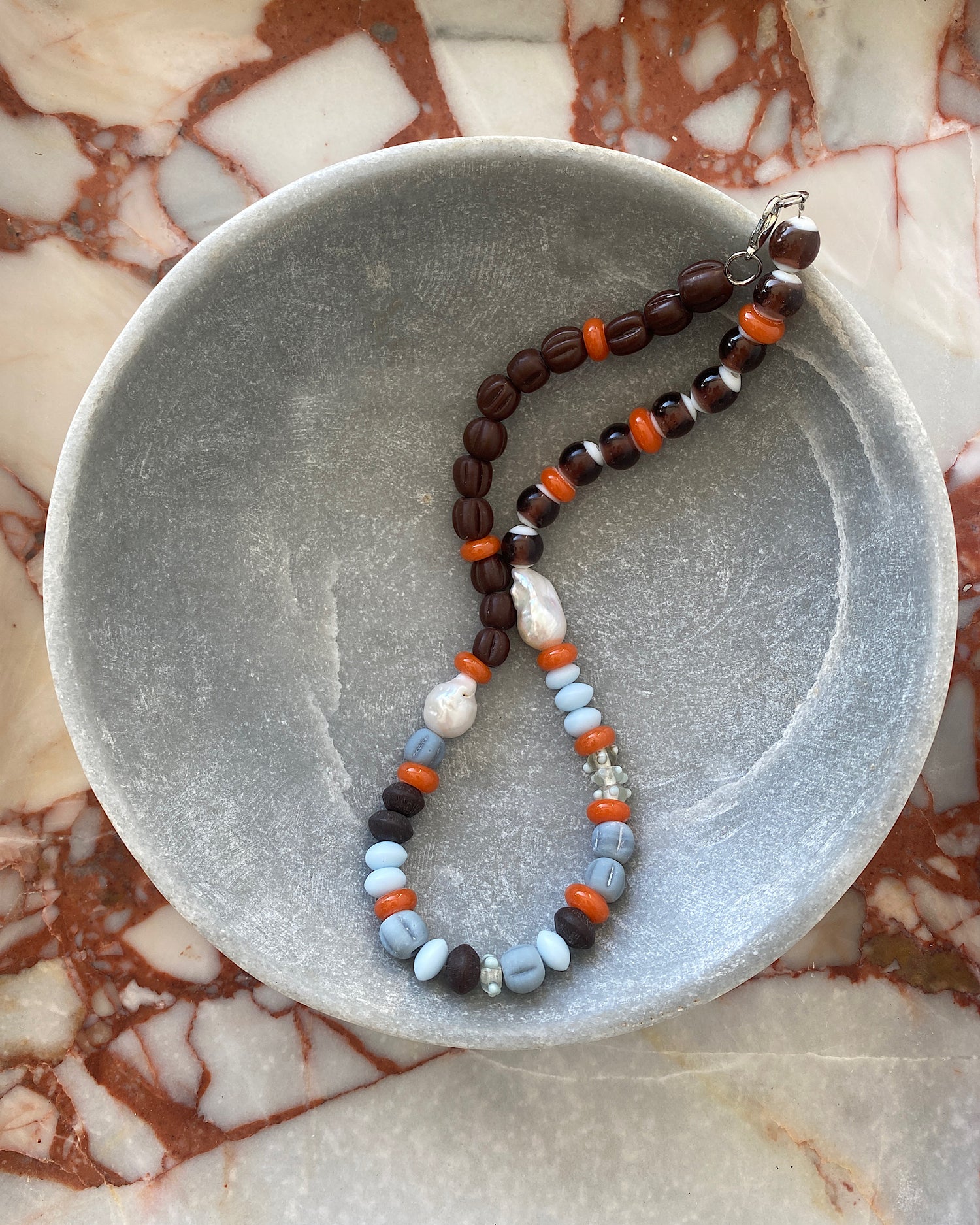 Earth toned assorted beaded glass and pearl necklace in a stone bowl on marble