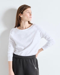 Woman wearing a white long-sleeve top and black pants against a light gray background