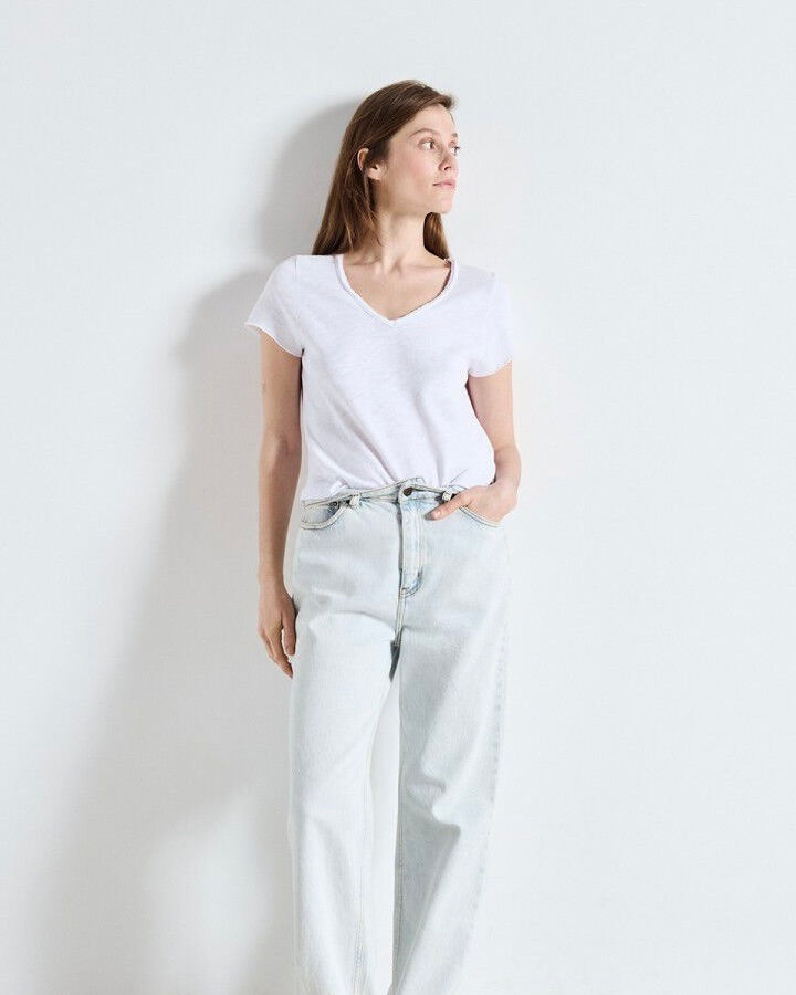 Woman wearing a white t-shirt and light blue jeans against a plain background
