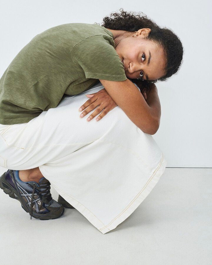 Person sitting on a white floor wearing a green shirt and white pants.
