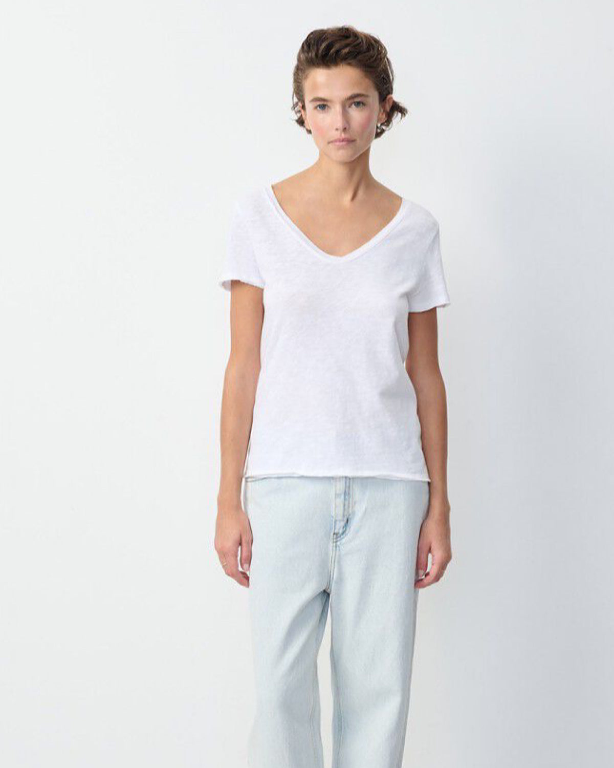 Person wearing a white v neck t-shirt and light blue jeans on a plain background