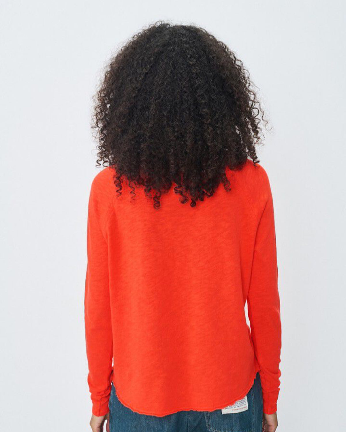 Person wearing an orange long-sleeve shirt with a plain background 