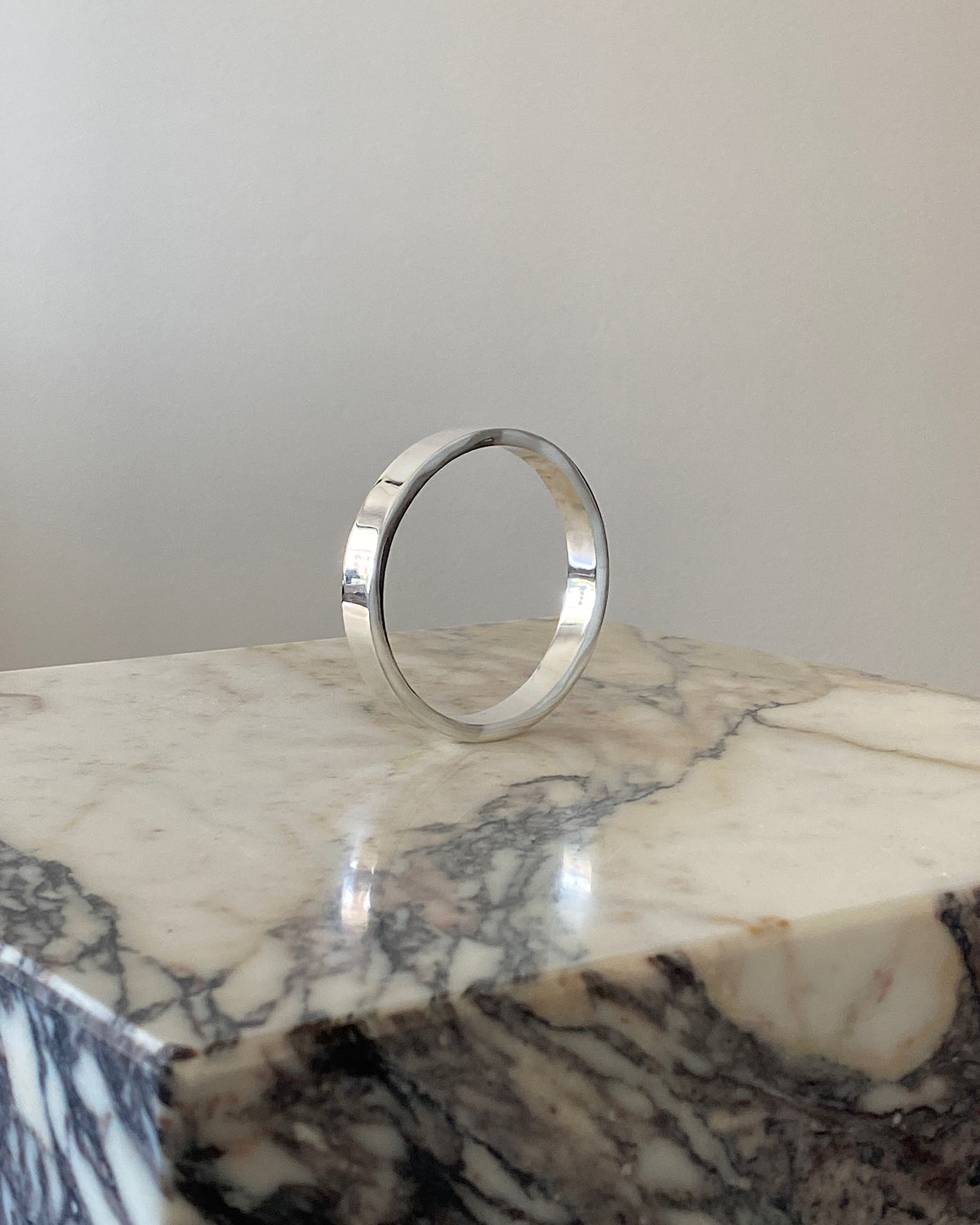 a classic square edged round silver bangle sits on a marble plinth