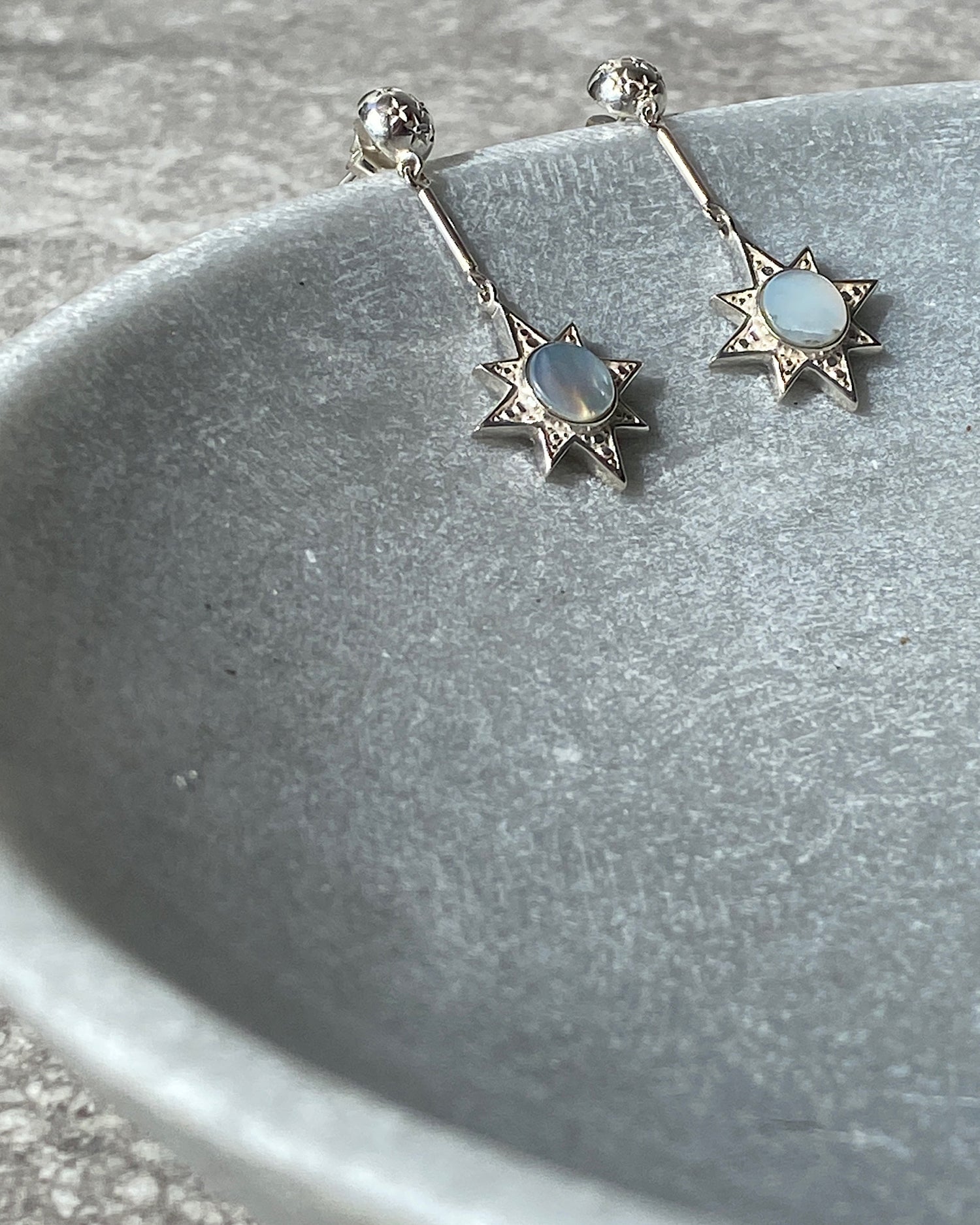 silver star drop earrings sit in a stone bowl