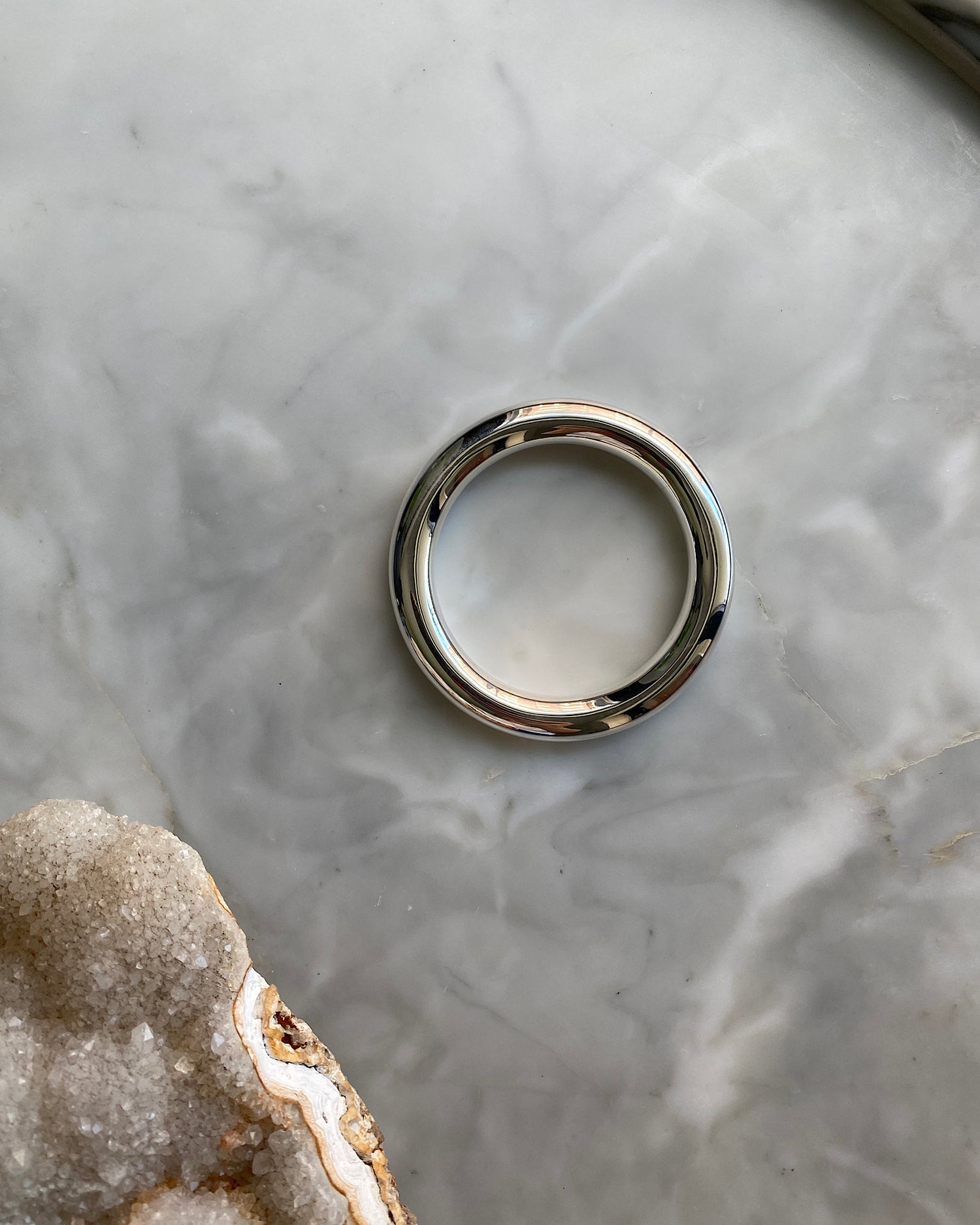 wide tube like sterling silver bangle sits on marble