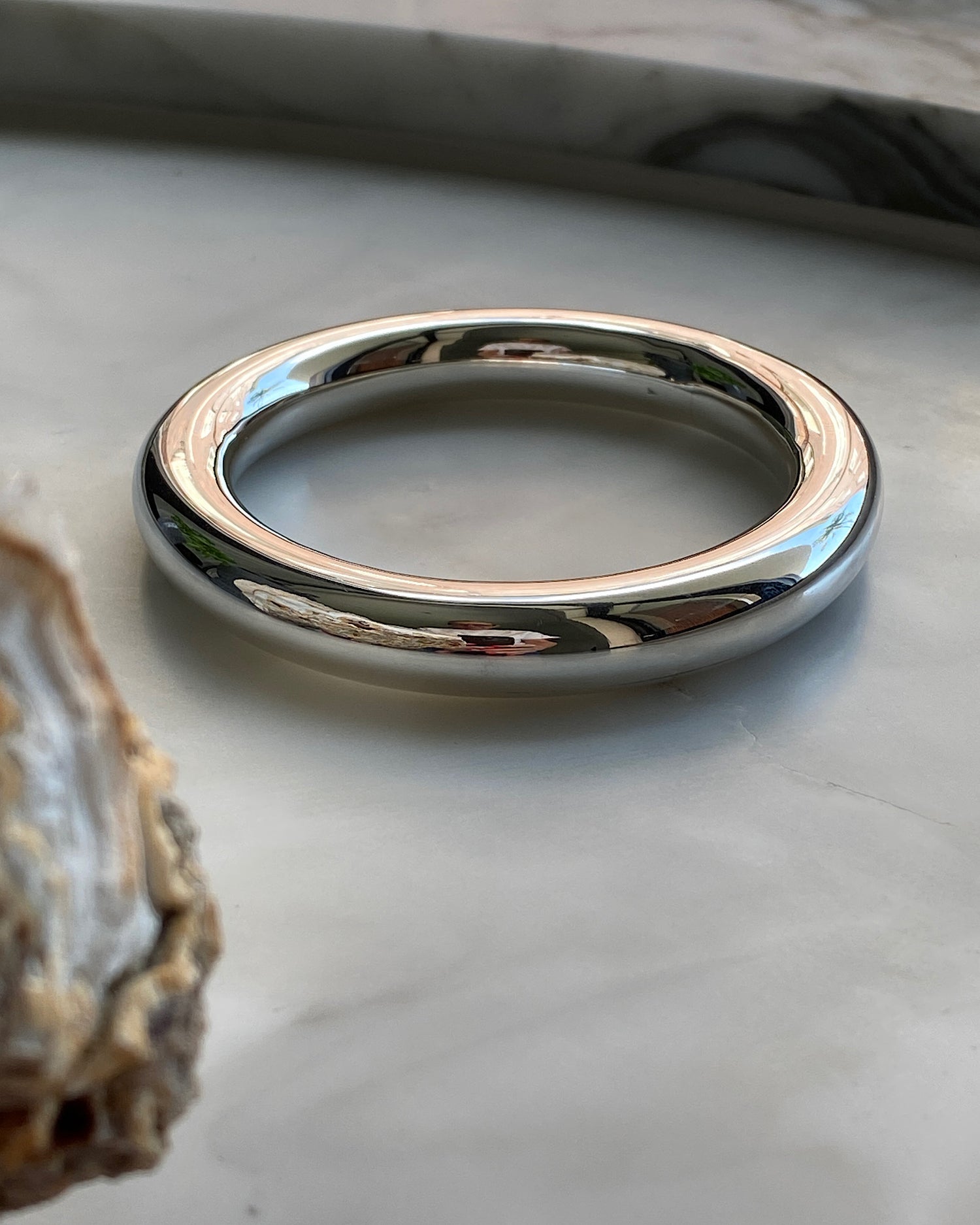 wide tube like sterling silver bangle sits on marble