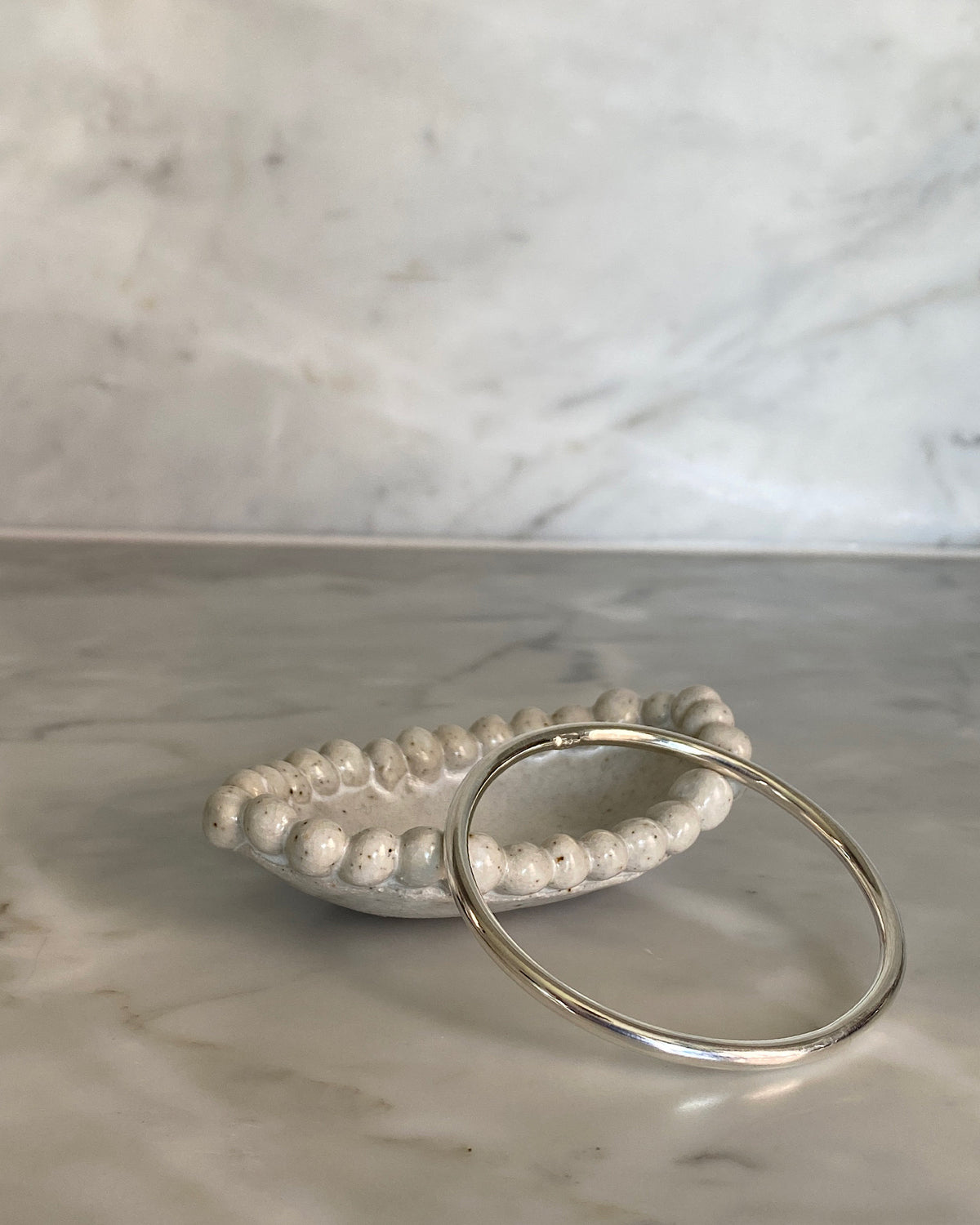 thin sterling silver simple bangle sits on a ceramic dish