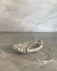 thin sterling silver simple bangle sits on a ceramic dish