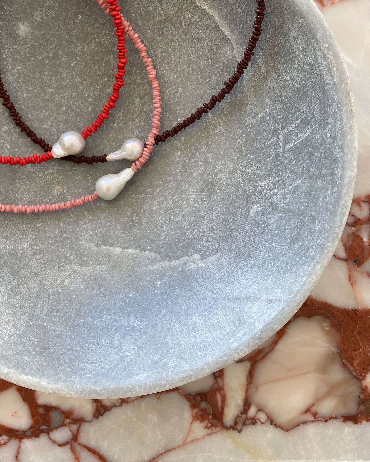 a simple baroque pearl sits on a chocolate, red or pink beaded necklace