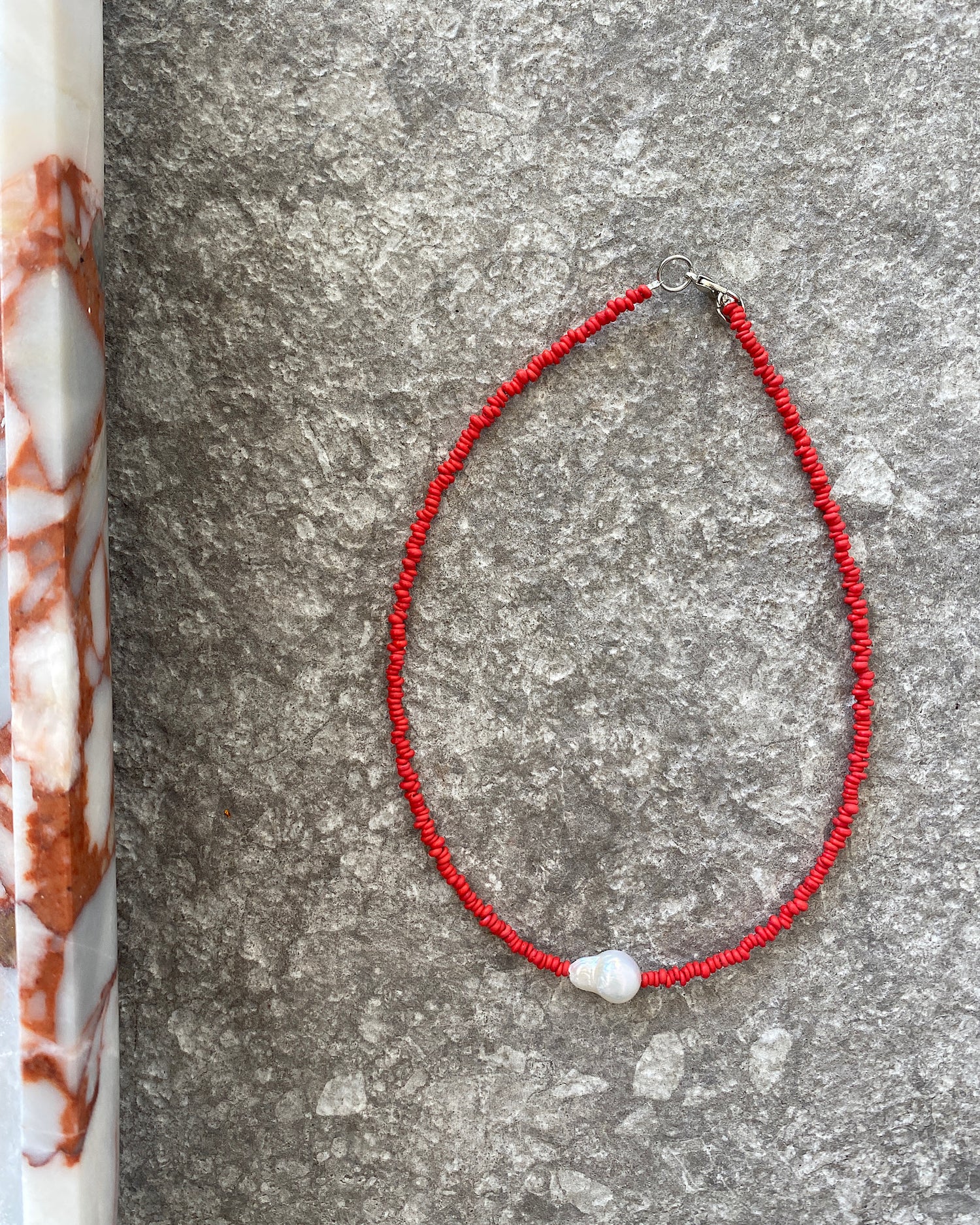 a single baroque pearl floats on a red bead necklace