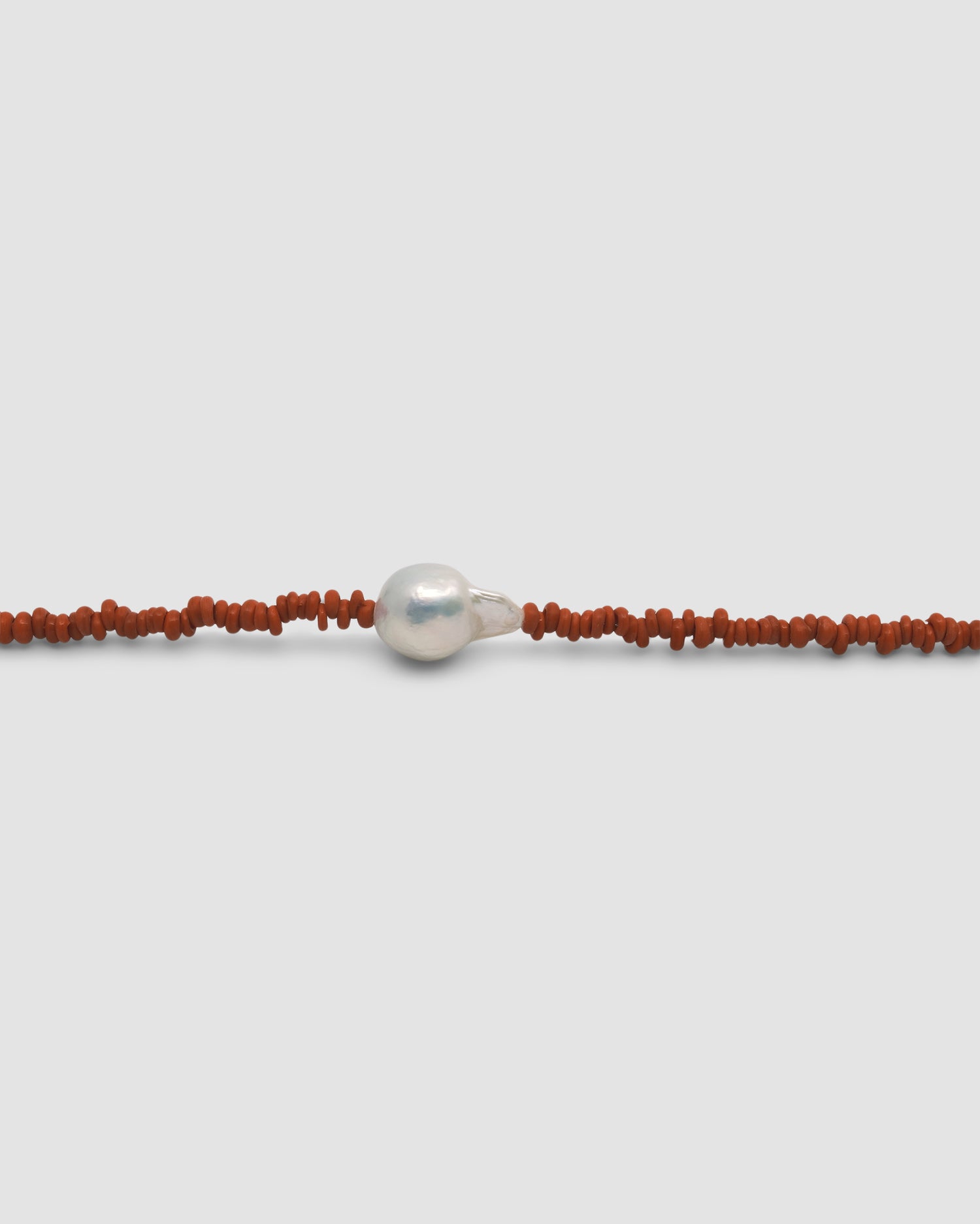 a single baroque pearl floats on a red bead necklace